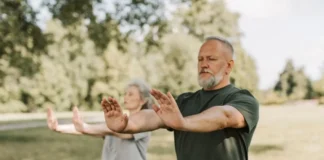 Dos personas adultas practican Tai Chi al aire libre en un parque, una actividad suave y de bajo impacto adecuada para mejorar equilibrio y movilidad.