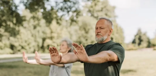 Dos personas adultas practican Tai Chi al aire libre en un parque, una actividad suave y de bajo impacto adecuada para mejorar equilibrio y movilidad.