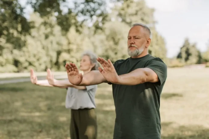 Dos personas adultas practican Tai Chi al aire libre en un parque, una actividad suave y de bajo impacto adecuada para mejorar equilibrio y movilidad.
