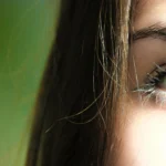 Perfil de una chica, muestra solo un ojo, el otro queda ocultado. Tiene los ojos de color verde y una melena lacia.