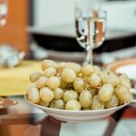 Un plato de uvas verds y en una mesa y una copa que las acompaña