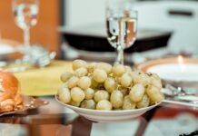 Un plato de uvas verds y en una mesa y una copa que las acompaña