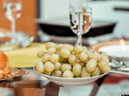 Celebrar la nochevieja con diabetes, ¿puedo comer las uvas? Un plato de uvas verds y en una mesa y una copa que las acompaña
