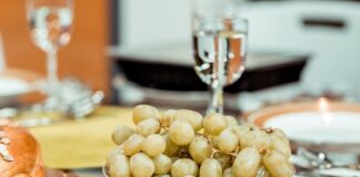 Un plato de uvas verds y en una mesa y una copa que las acompaña
