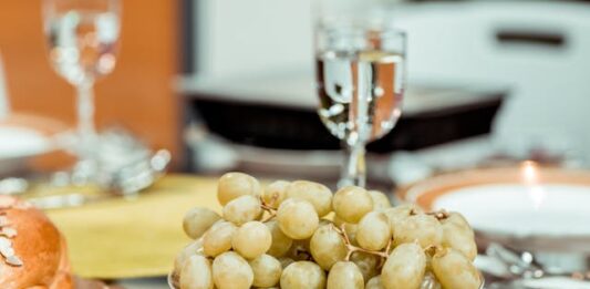 Un plato de uvas verds y en una mesa y una copa que las acompaña