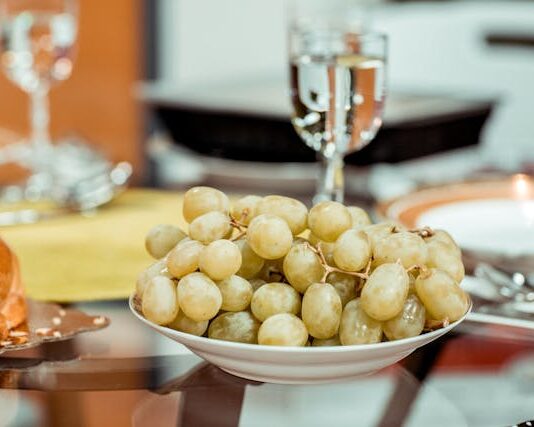 Un plato de uvas verds y en una mesa y una copa que las acompaña