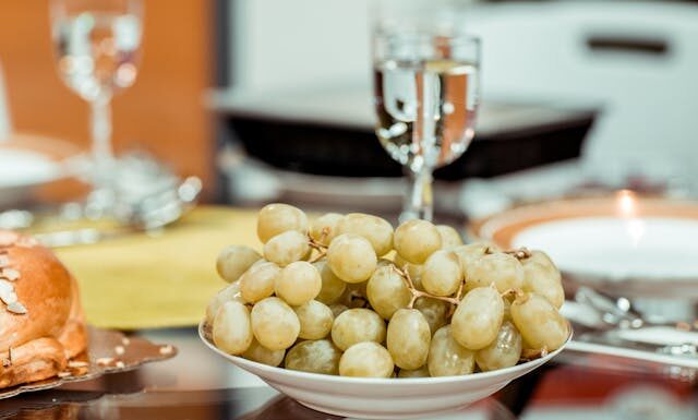 Un plato de uvas verds y en una mesa y una copa que las acompaña